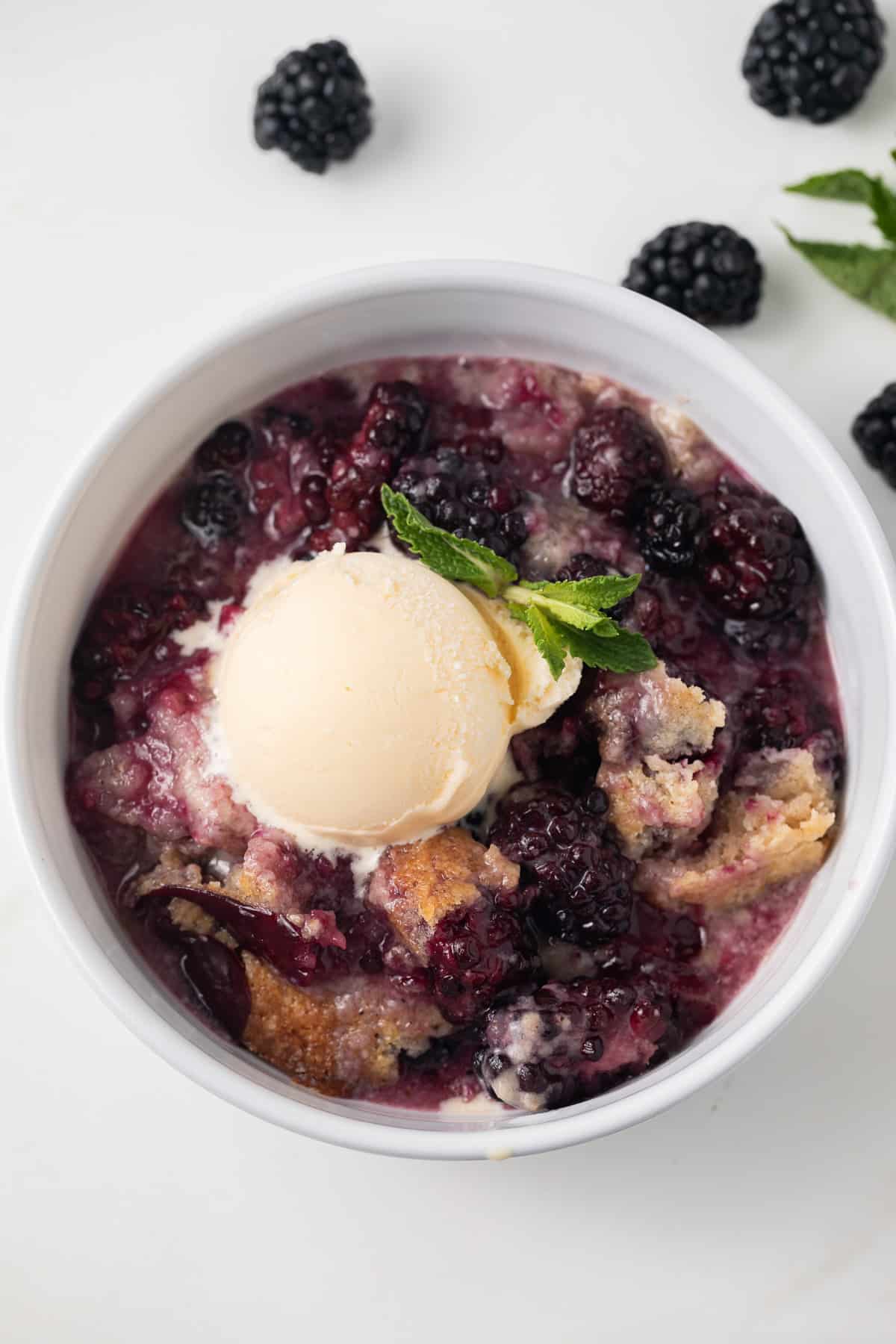 Blackberry cobbler in white bowl with scoop of vanilla ice cream.