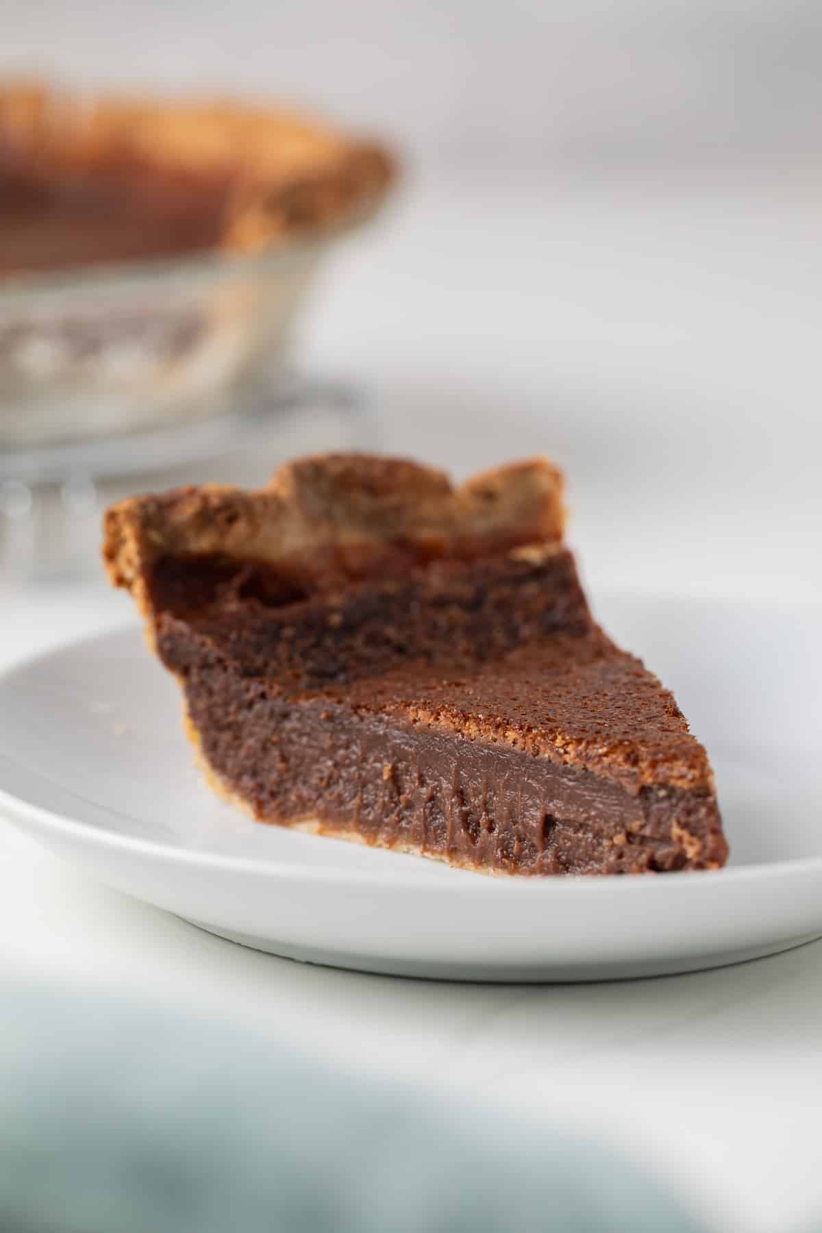 Side view of a slice of chocolate chess pie on white plate.