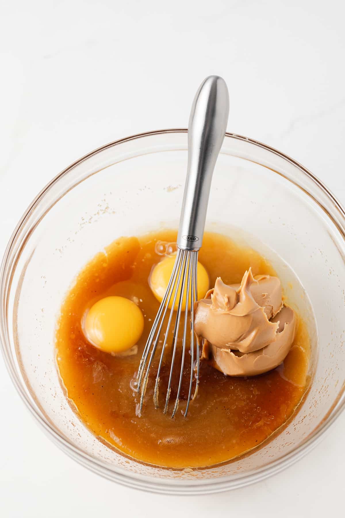 Peanut butter, eggs, vanilla in glass mixing bowl.