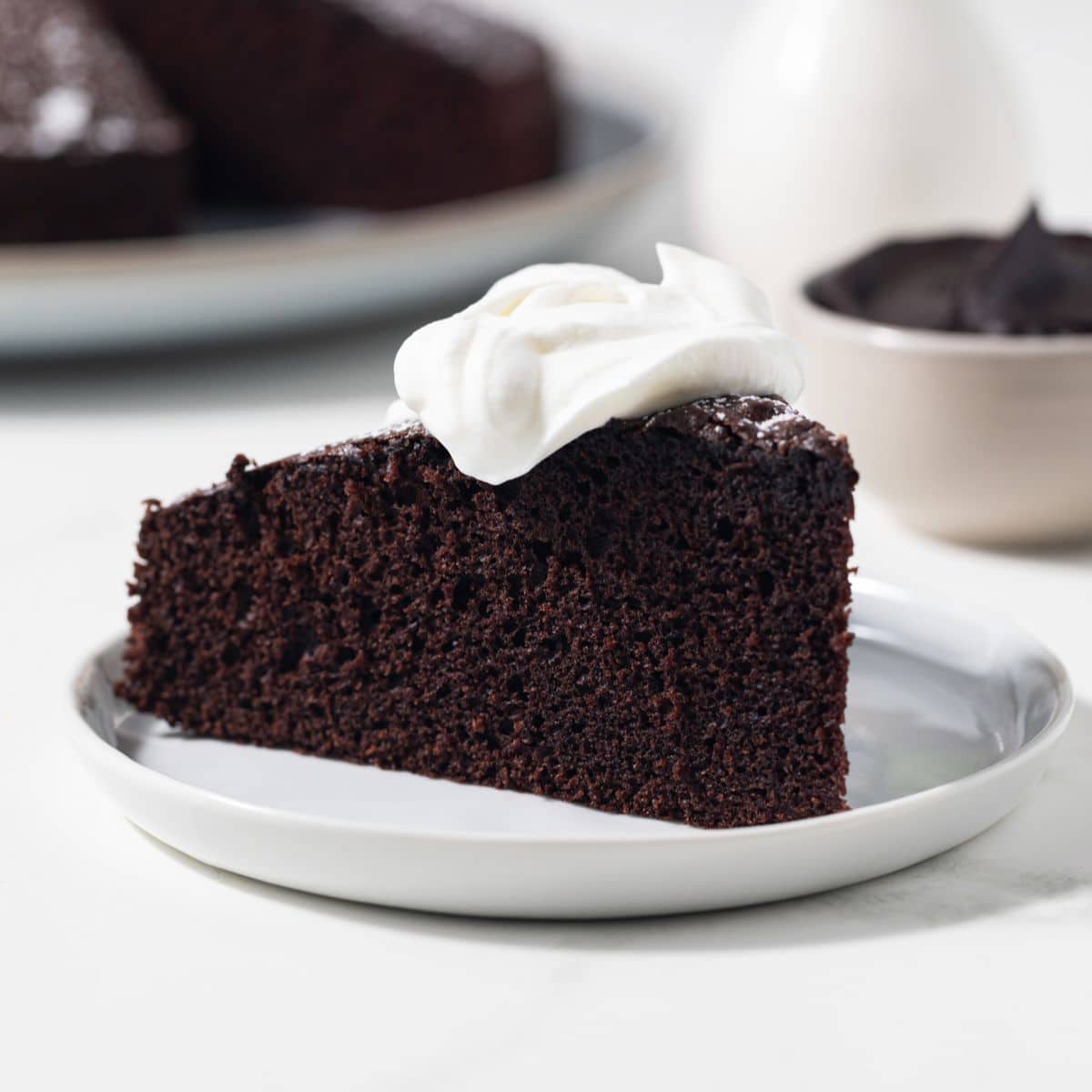 Slice of chocolate olive oil cake with whipped cream on top.