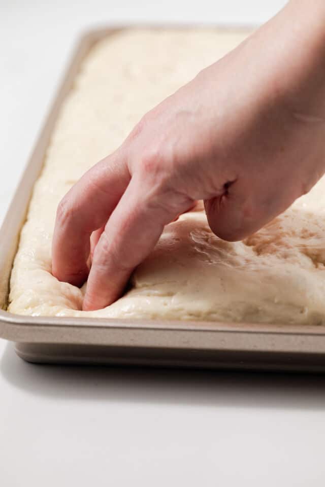 Fingertips dimpling dough in baking dish.