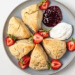 Plate of cream scones with strawberries, jam, and whipped cream.