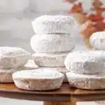 Powdered sugar donuts on a wooden cake stand.