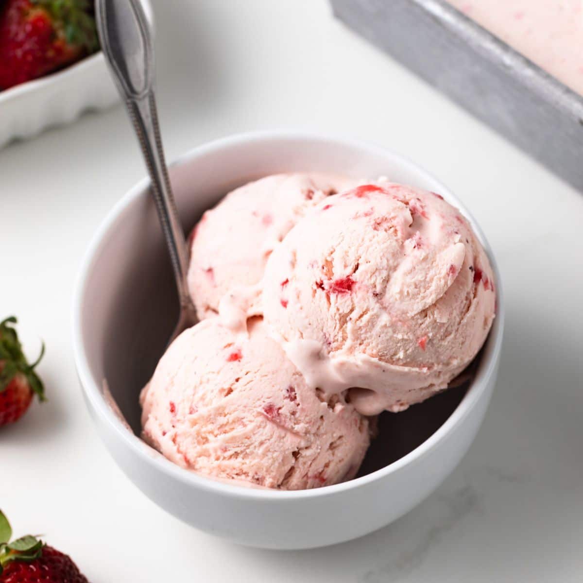 Strawberry ice cream in a bowl with a spoon.