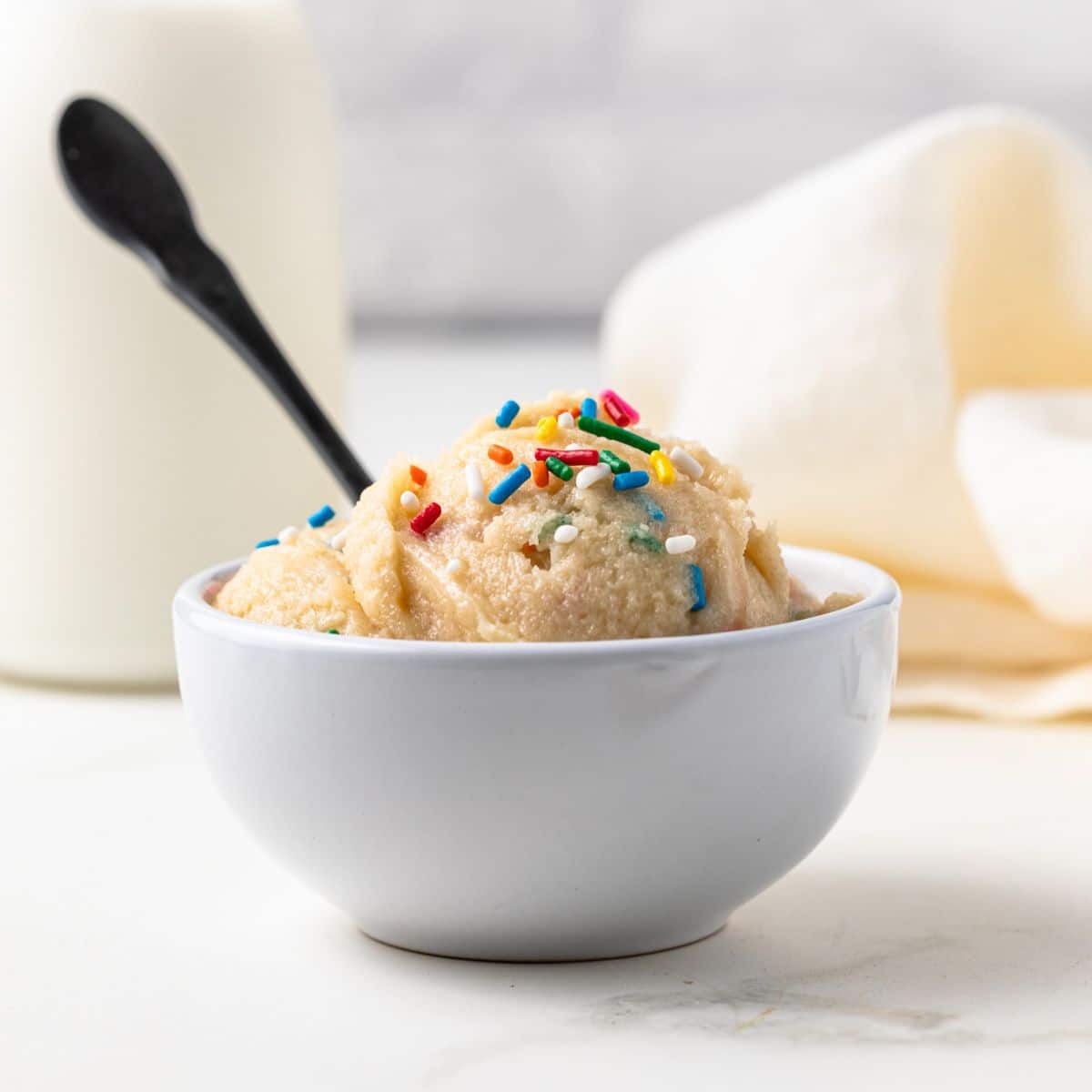 Side view of edible cookie dough in white bowl.