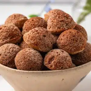 Side view of baked apple cider donut holes in bowl.