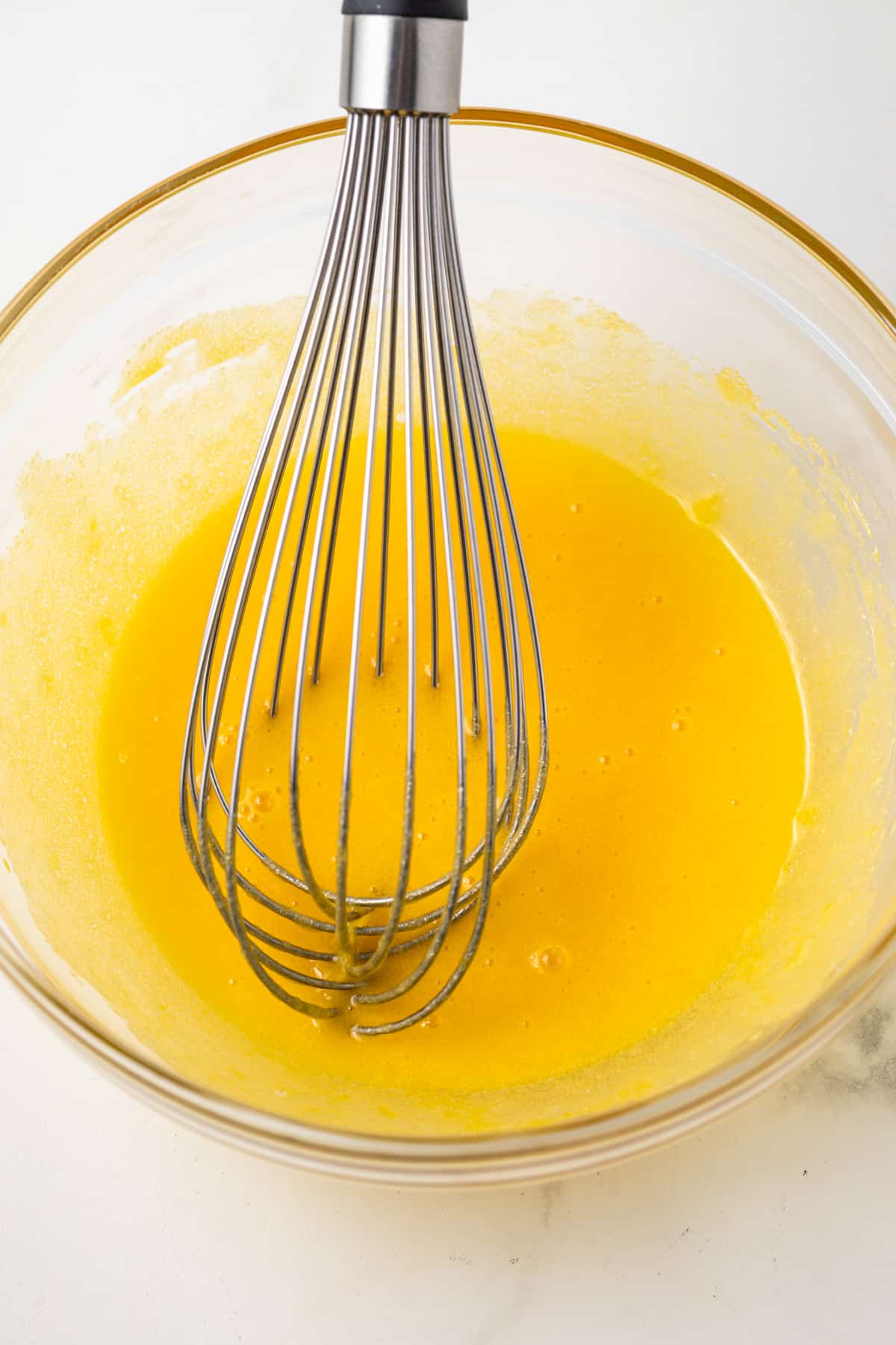 Eggs mixed with sugar in glass bowl.