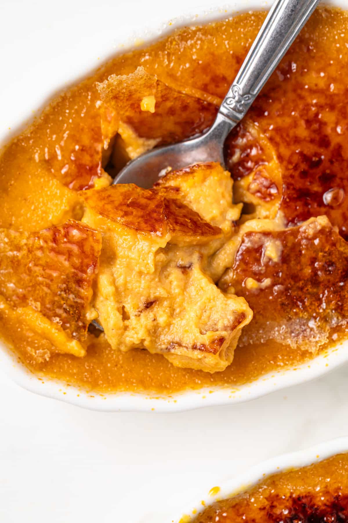 Close up of spoon breaking sugar topping on pumpkin creme brulee.