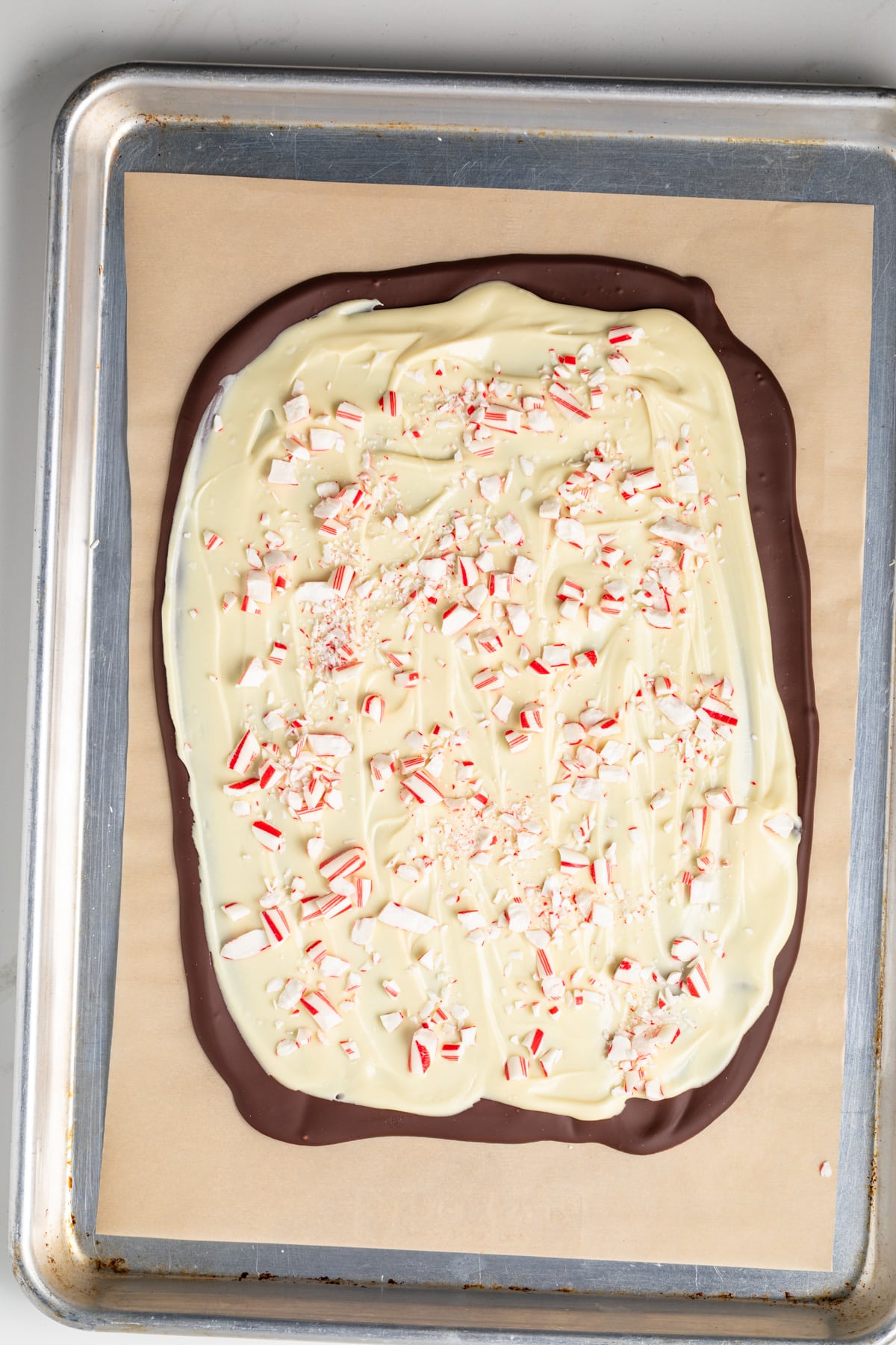 Chocolate, white chocolate, and crushed candy canes spread on parchment paper.