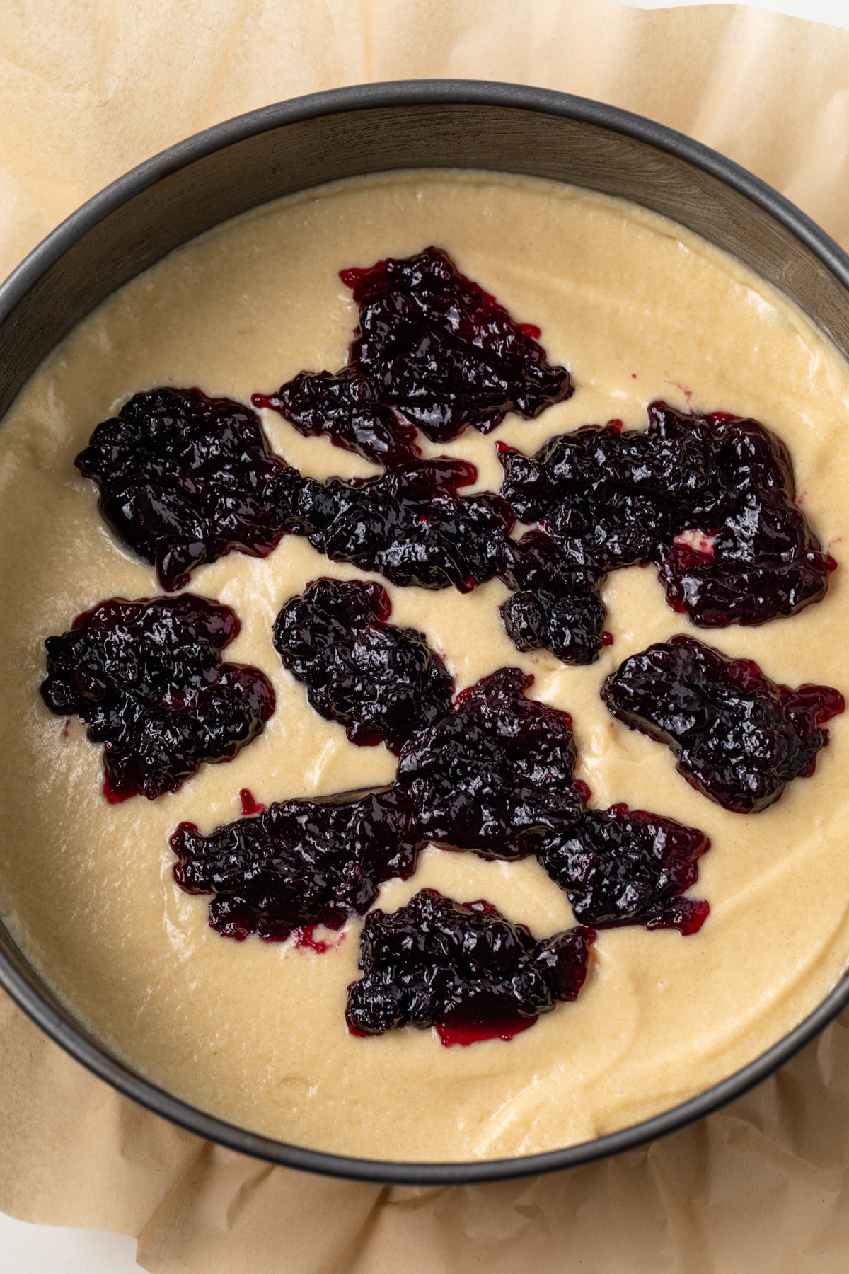 Coffee cake batter in a round pan with blueberry jam over the top.