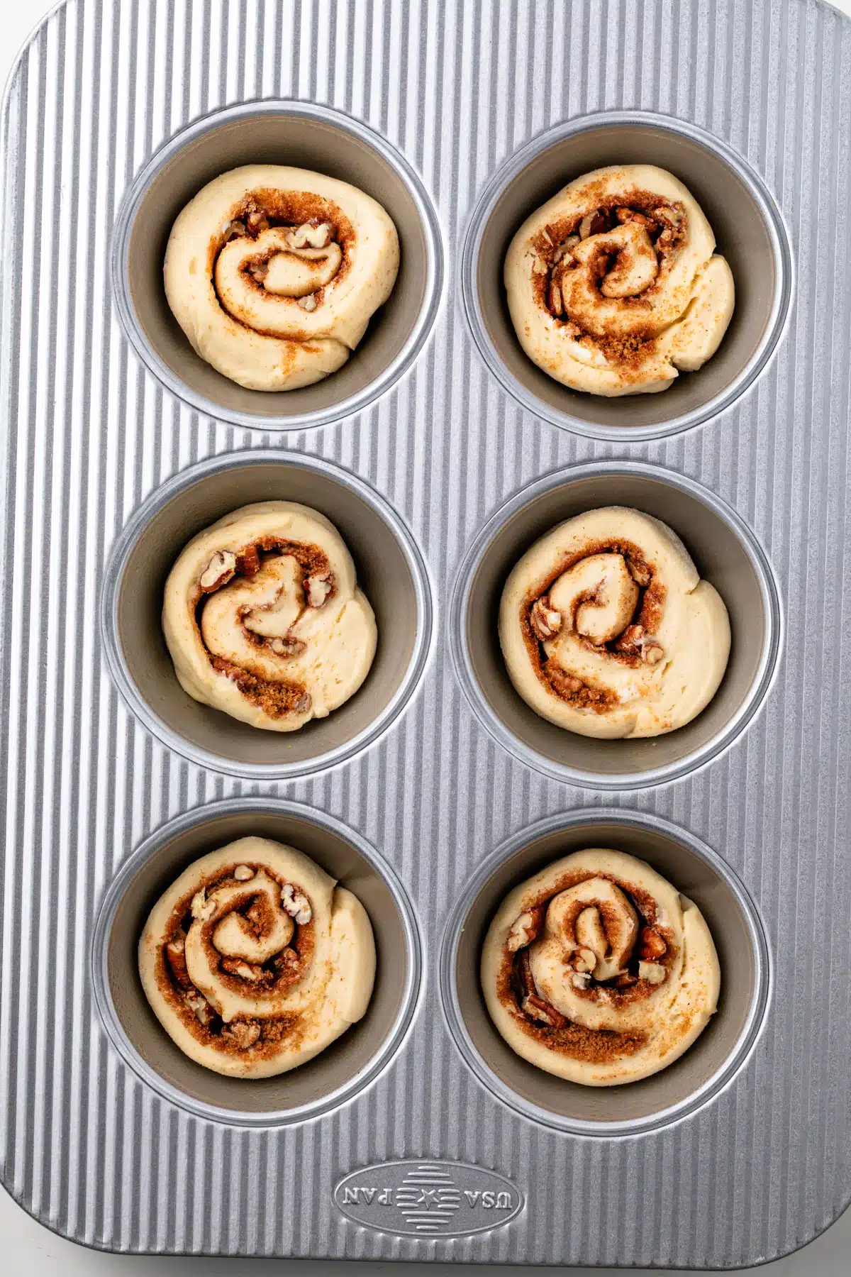 Unbaked pecan rolls in a large muffin pan.