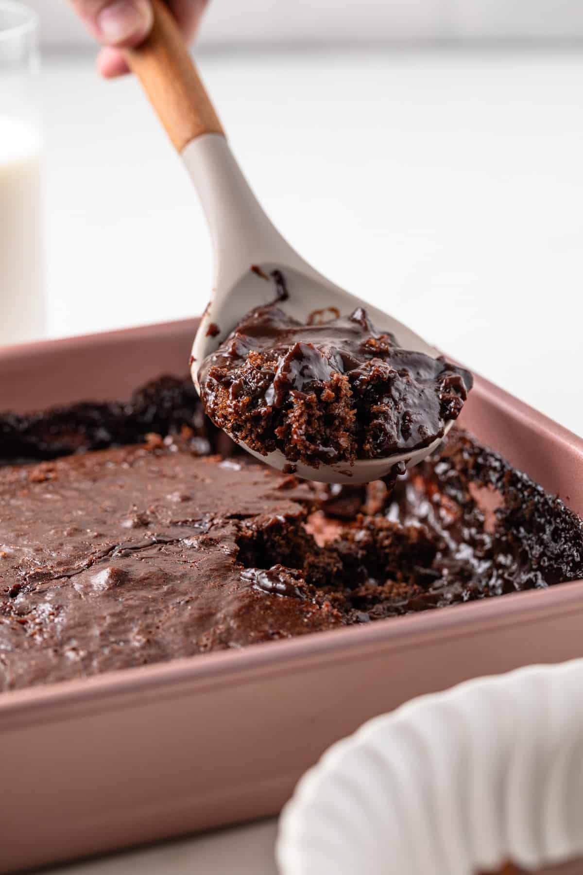 A spoonful of chocolate pudding cake being lifted from a baking dish.