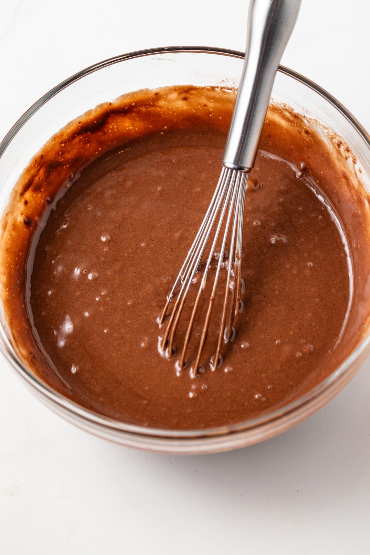 Chocolate pudding cake batter in a glass mixing bowl with a whisk.