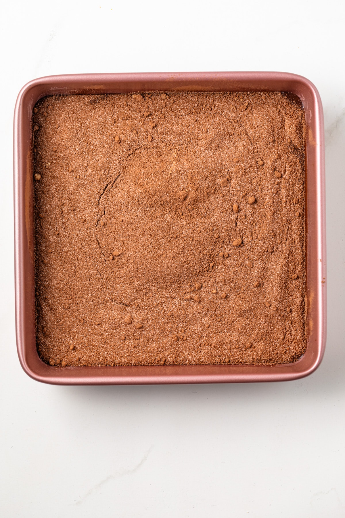 An overhead view of chocolate pudding cake batter topped with cocoa powder and sugar in a square baking dish.